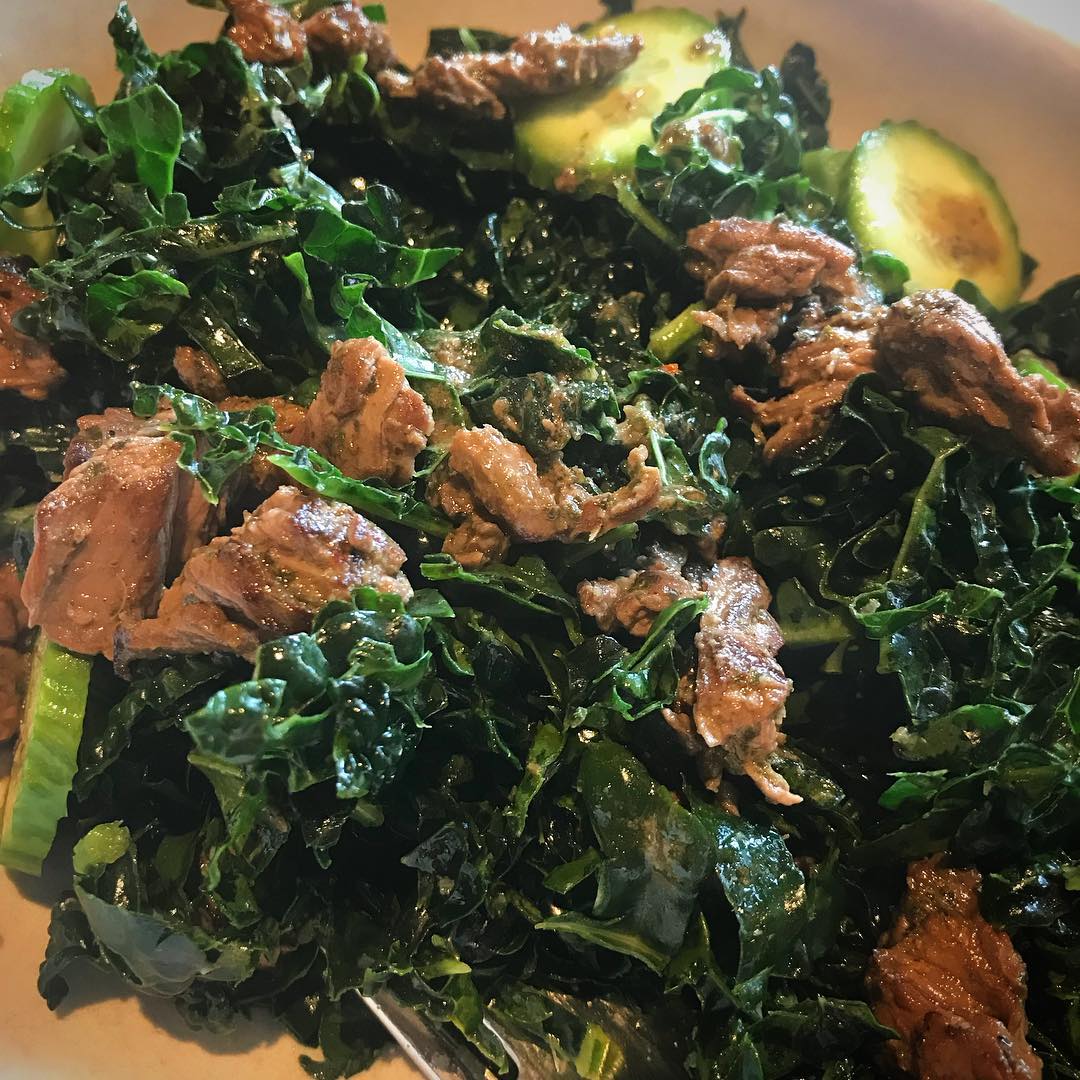 Shredded kale salad topped with grass-fed steak and cucumber—dressed with a litt…